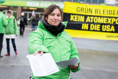 Bei einer Protestaktion verteilt eine Greenpeace-Aktivistin Info-Flyer; hinter ihr ein Banner mit der Aufschrift "Kein Atomexport in die USA".