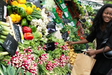 Eine Frau kauft Gemüse an einem Marktstand