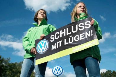 Zwei Greenpeace-Aktivistinnen in grünen Jacken stehen vor einem VW-Logo. Die beiden halten ein Banner mit der Aufschrift "Schluss mit Lügen!"; das Schild zeigt ebenfalls ein VW-Logo