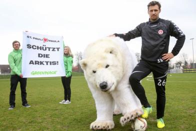 Sören Gonther, Mannschaftskapitän de FC St. Pauli, mit Eisbärdame Paula. Hinter ihnen fordern zwei Greenpeace-Aktivisten auf einem Banner: "Schützt die Arktis".
