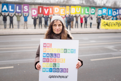 Greenpeace-Aktivisten bilden mit Buchstabentafeln die Worte "Walls devide. Build bridges" vorm Berliner Mauerdenkmal