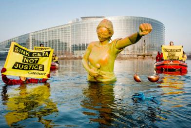 Greenpeace-Aktivisten im Schlauchboot versenken eine Statue von Justitia im Wasser, sie halten Banner "Stop Ceta"