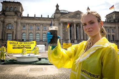 Aktivisten vor dem Reichstag in Berlin halten ein Banner mit der Aufschrift "Gülle im Wasser ist Scheiße! Politiker müssen handeln! Davor steht ein drei Meter großer mit Gülle gefüllter Suppenteller