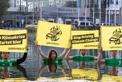 In einem 100 mal 90 Meter großen Wasserbecken stehend, halten Aktivist:innen Banner mit dem Slogan „Die Klimakrise startet hier“ sowie „Stop Driving Climate Change“.