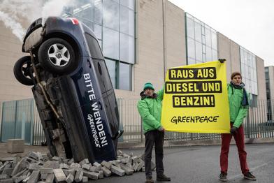 Mit einem schräg im Boden steckenden Auto demonstrieren Greenpeace-Aktivisten vor dem Bundeskanzleramt für Klimaschutz im Verkehr. Der Wagen mit qualmendem Auspuff trägt die Aufschrift „Bitte wenden!“