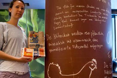 Frau steht neben McDonald's-Werbetafel. Darauf steht: „Die Hähnchen werden ohne genmodifizierte Futtermittel aufgezogen.“