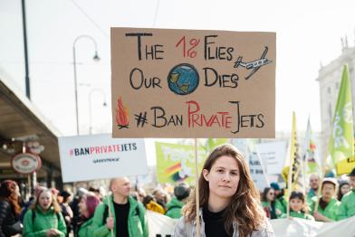 Klimastreik: Frau hält Schild "The 1 % Flies, Our Planet Dies. #BanPrivateJets"