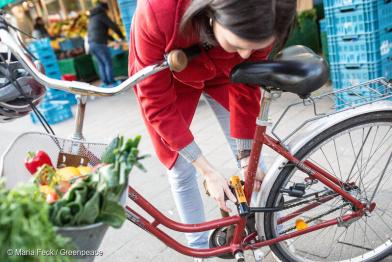 Frau schließt Fahrrad auf, im Korb ist Gemüse und Obst
