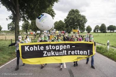 5 Greenpeace Jugendliche tragen ein gelb/schwarzes Banner mit weißer Schrift: Kohle stoppen Zukunft retten! 