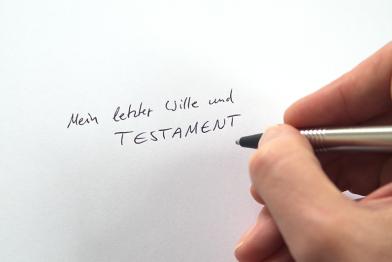 Eine Hand schreibt "Mein letzter Wille und Testament" auf ein Blatt Papier.