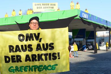 Knapp 20 Greenpeace-Aktivisten stehen auf dem Dach und dem Gelände einer OMV-Tankstelle. Im Vordergrund hält einer der Aktivisten ein Banner mit der Aufschrift "OMV, raus aus der Arktis!"
