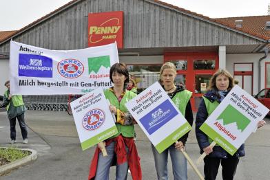 Ehrenamtliche halten Protestschilder gegen Gen-Milch.