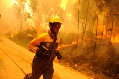 Ein Feuerwehrmann läuft eine Straße entlang; hinter ihm brennt der Wald.