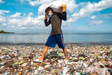 Mann trägt Müllsack über völlig verdreckten Strand von Manila