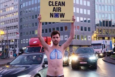 Aktivist mit nacktem Oberkörper auf dem eine blaue Lunge gemalt ist, hält ein Banner: Clean Air Now