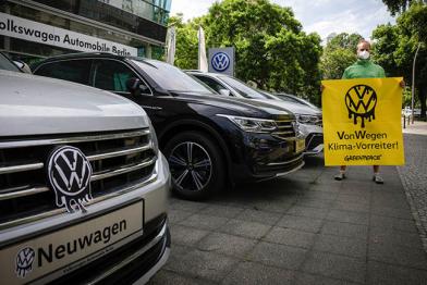 Aktivist steht vor einem VW-Händler und hält ein Banner mit der Aufschrift "Von Wegen Klima-Vorreiter!"