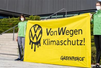 Zwei Aktivist:innen halten ein Banner "Von Wegen Klimaschutz" vor der VW-Hauptversammlung in Berlin.