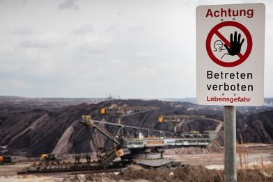 Braunkohle Tagebau von Vattenfall in der Lausitz. Ein Schaufelradbagger steht in einer Tagebaugrube. Warnschild von Vattenfall im Vordergrund.