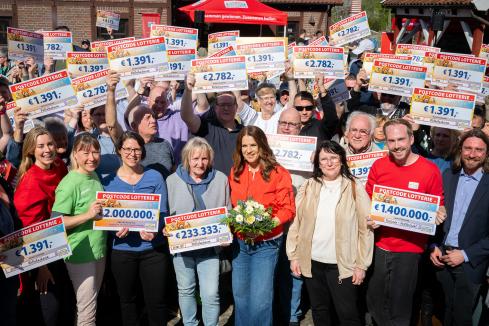 Viele Gewinner:innen der Deutschen Postcode Lotterie zeigen ihre großen Gewinn-Schecks.