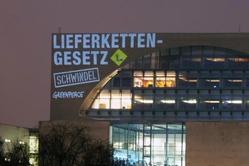 Auf das Bundeskanzleramt projizieren Greenpeace Aktivist:innen die Botschaft “Lieferkettengesetz - Schwindel” mit einem Zeichen für Umweltgefahren. 