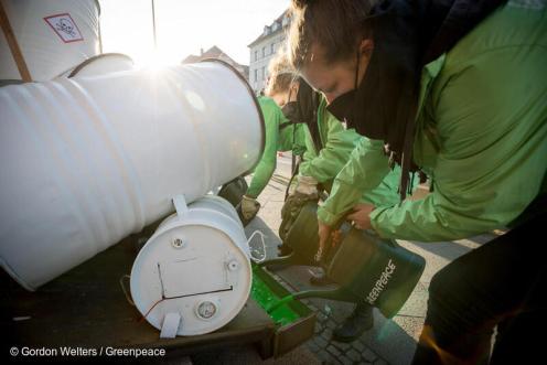 Greenpeace Aktivist:innen gießen grüne Flüssigkeit aus Gartengießkannen , daneben stehen weiße Chemie-Tonnen
