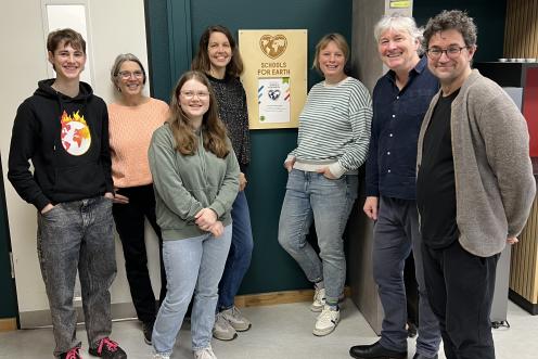 Sieben Personen stehen neben an der Wand hängenden Schullabel und lächeln in die Kamera