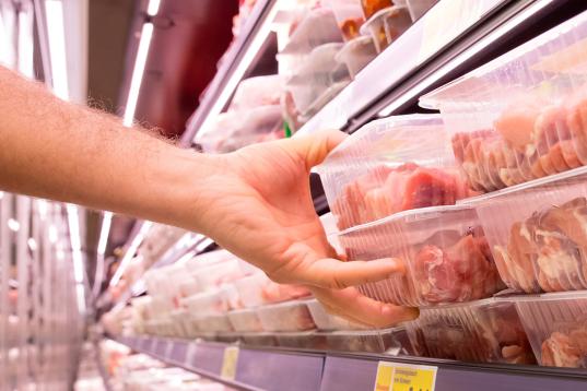 Eine Hand greift zu einer im Kühlregal liegenden Fleischpackung.