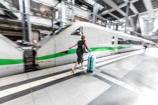 Frau läuft mit Rollkoffer auf einem Bahnsteig am ICE entlang