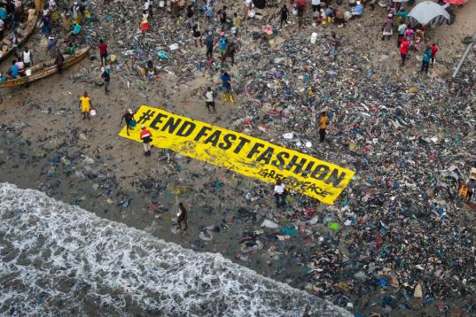 Großes Banner "End Fast Fashion" liegt am Strand in Ghana zwischen Textilmüll.
