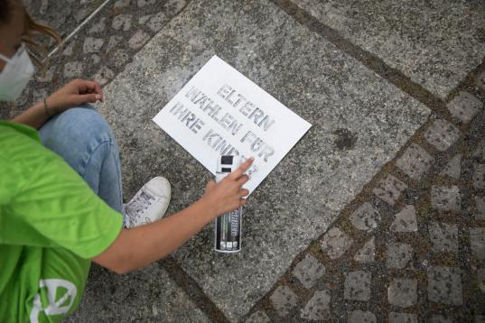 Junge Greenpeace-Aktivist:innen demonstrieren für Klimaabstimmung in Berlin. Mit Sprühkreide schreiben sie "Eltern wählen für ihre Kinder" auf den Boden. Mit einem 6 x 30 m großen Schriftzug aus einzelnen Stoffbuchstaben platzieren sie die Worte "Klima" "#vote 4 me" und ein überdimensionales Wahlkreuz auf dem Reichstagsrasen.