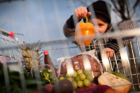 Kind schaut durch einen Einkaufskorb, in dem Obst liegt.