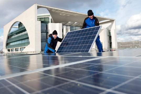 Arbeiter installieren Photovoltaikanlage auf Dach vor Reichstag in Berlin