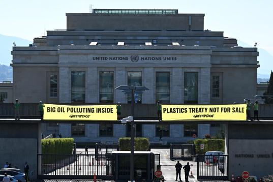 Vor dem UN-Gebäude hängen Greenpeace-Aktive zwei Banner "Big oil polluting inside",  "Plastics treaty not fpr sale".