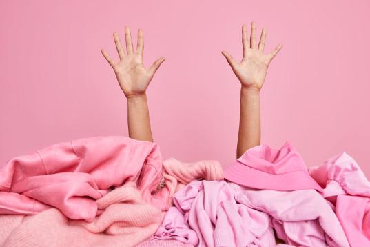 Nach oben gereckte Arme hinter einem rosa Kleiderhaufen