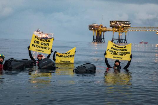 Greenpeace-Aktivisten schwimmen mit Banner und Gepäck zur Ölplattform