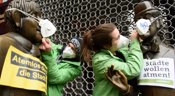 Greenpeace-Aktivisten setzen Tünnes und Schäl in der Kölner Altstadt Atemschutzmasken auf.
