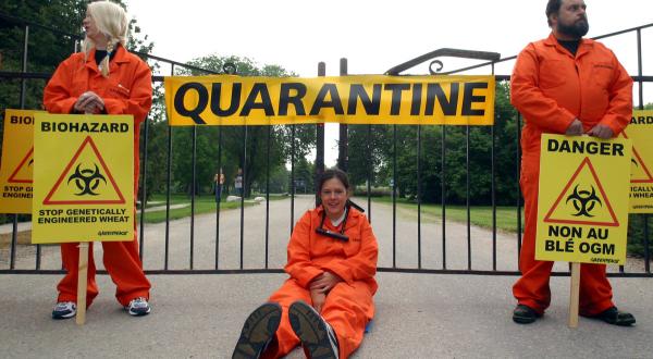 Aktivistin kettet sich am Tor der Versuchsfarm in Morden, Kanada, fest. Am Eingangstor hängt ein Banner mit der Aufschrift "Quarantäne".