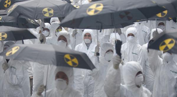 Aktion zum Fukushima-Jahrestag: Greenpeace Aktivist:innen, die Strahlenschutzanzüge und Masken tragen, ziehen durch einige der belebtesten Orte Jakartas, um auf die Gefahren der Kernenergie hinzuweisen. Sie halten auch schwarze Regenschirme mit Nuklearsymbolen in der Hand. 