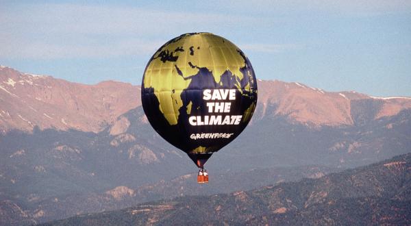 Heißluftballon mit der Aufschrift " Rettet das Klima" von Greenpeace fliegt über Berge.