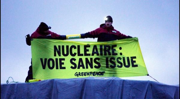 Greenpeace Aktivist:innen sind an einen Lastwagen gekettet, der einen Deckel für ein Kraftwerk transportiert, und zeigen Banner mit der Aufschrift "Atomkraft, Sackgasse"