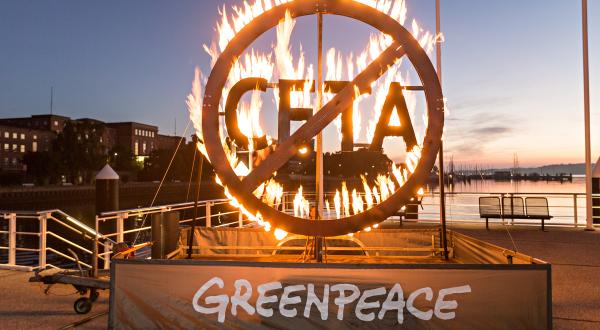 Greenpeace-Aktivist:innen demonstrieren mit einem brennenden CETA-Schild vor dem Kieler Landtag für mehr Widerstand gegen das europäisch-kanadische Handelsabkommen (CETA).