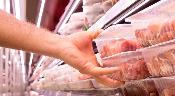 Eine Hand greift zu einer im Kühlregal liegenden Fleischpackung.
