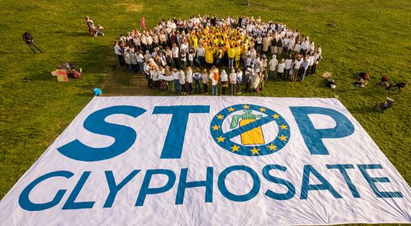 Menschen formen eine Blume, im Vordergrund ein großes Banner "Stop Glyphosate"