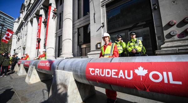 Klimaschützer:innen haben eine riesige Ölpipeline um das Gebäude gebaut. Sie trägt den Namen "Crudeau Öl". Kletterer:innen haben an zwei Eingangssäulen Banner mit der Aufschrift "Crudeau Öl Hauptquartier" heruntergelassen. 