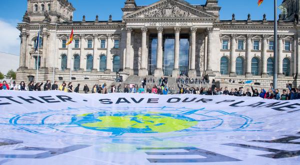 Jugendliche entfalten vor dem Reichstagsgebäude ein 15 Meter langes Banner mit der Weltkugel, eingebettet in einen Kompass. Auf dem Banner steht: "Rettet unseren Planeten. Gemeinsam Zukunft gestalten".