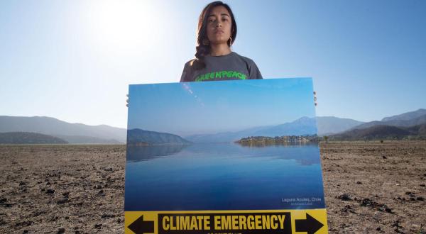Greenpeace Aktivist:innen protestieren in einer ausgetrockneten italienischen Lagune für Klimaschutz. Sie zeigen Bilder des Sees, als er noch mit Wasser gefüllt war. 