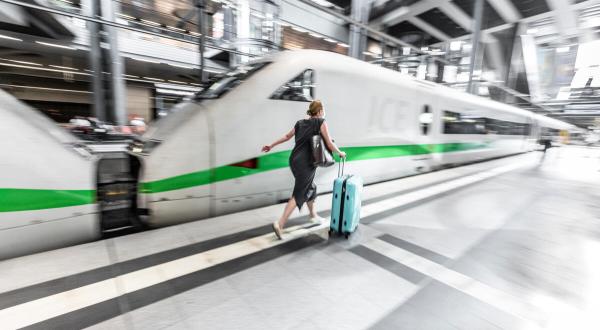 Frau läuft mit Rollkoffer auf einem Bahnsteig am ICE entlang
