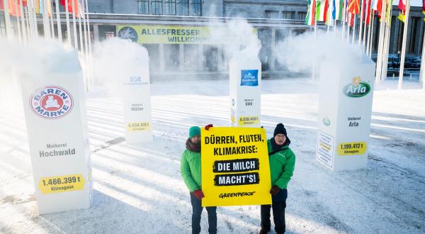 Vier überdimensionale Milchtüten stehen als Installation vor dem Eingang zur Internationalen Grünen Woche, begleitet von den Umweltaktivist:innen mit Transparenten: "Klimakrise: Die Milch macht's!" 