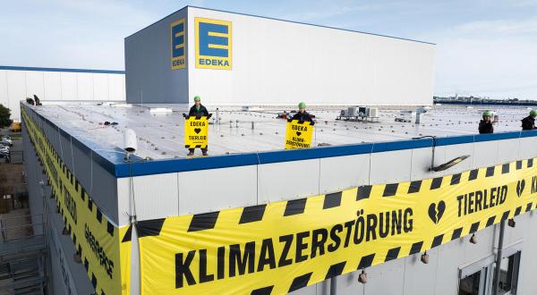 Vom Dach des Edeka-Werkes hängen fünf lange Banner in Absperrband-Optik mit der Warnung: “Tierleid und Klimazerstörung”.