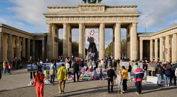  Passant:innen betrachten Kleiderstatue aus Textilmüll vor dem Brandenburger Tor